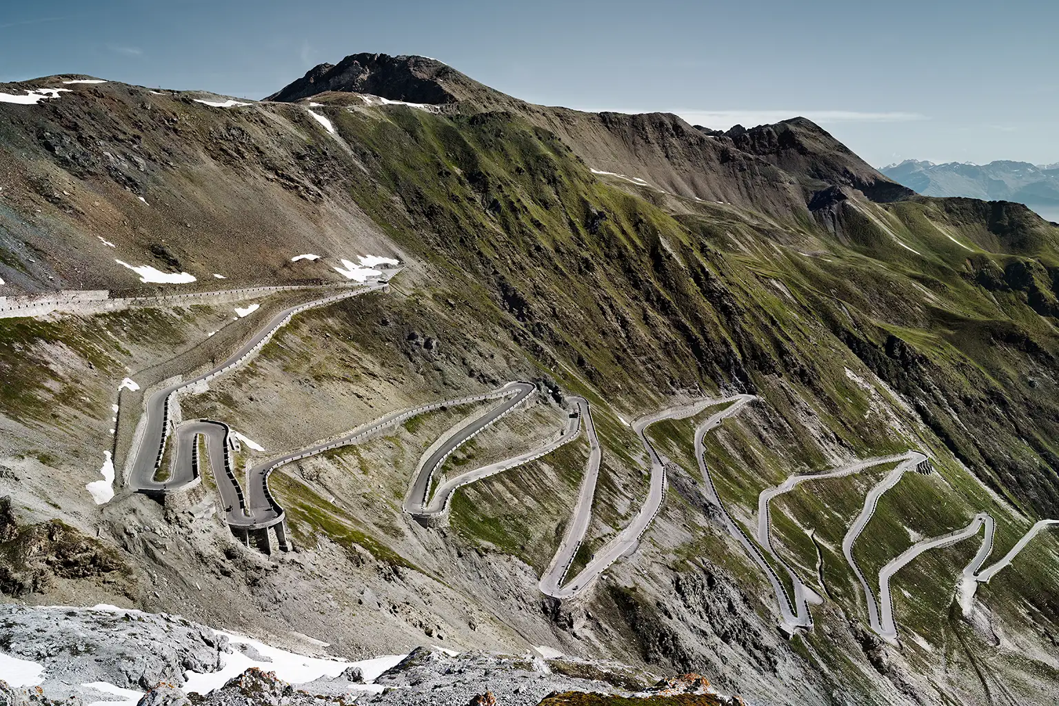Blick auf die Ostrampe der Stilfser-Joch-Straße mit zahlreichen Serpentinen im Morgenlicht; historische Alpenstraße mit steiler, kurvenreicher Trassenführung.